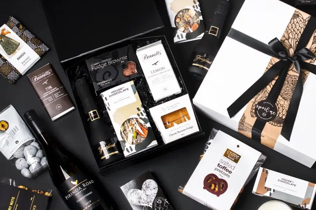 Elegant black gift box filled with assorted chocolates, wine bottles, and gourmet treats arranged neatly on a dark surface.
