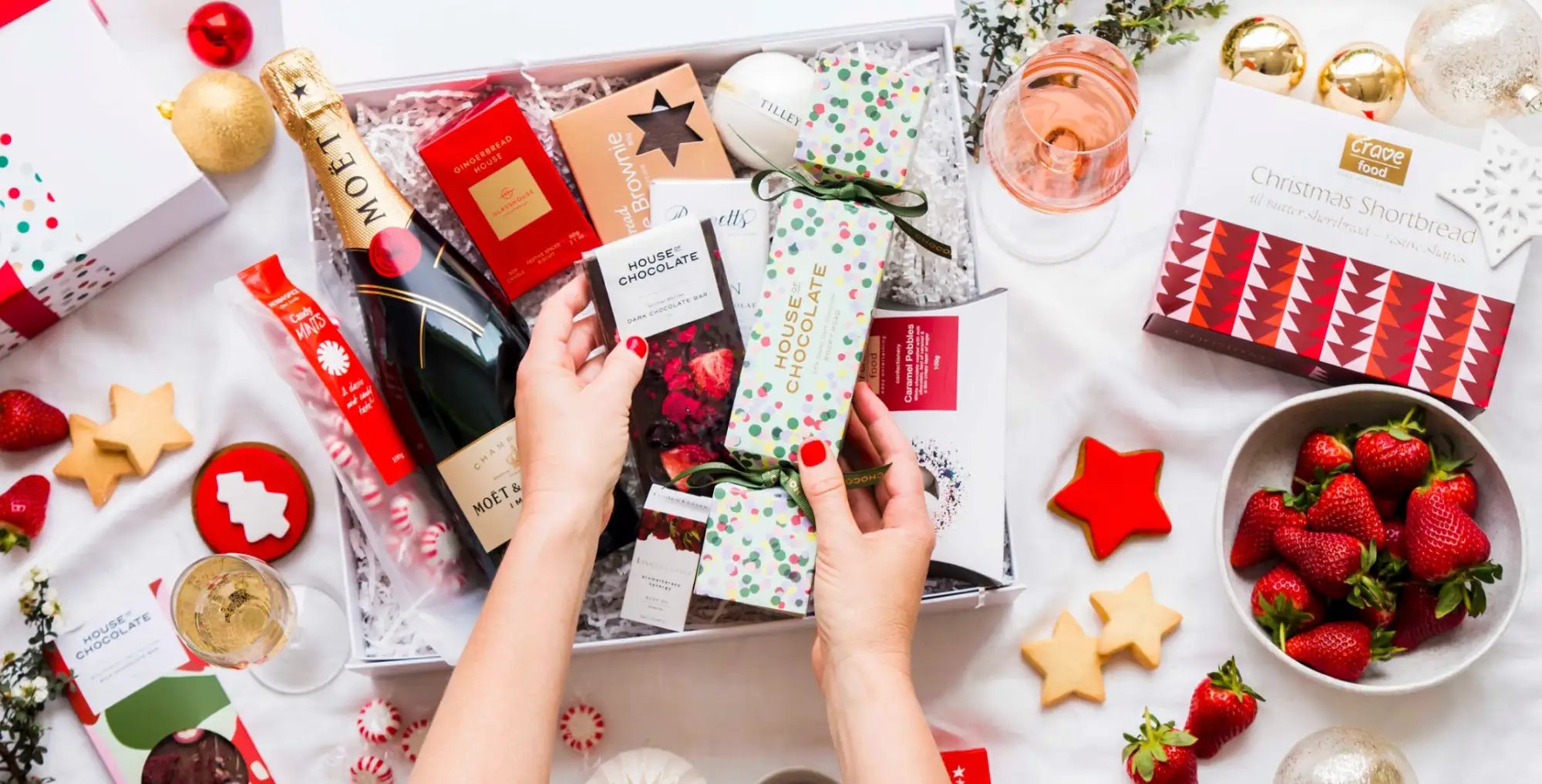 A festive gift box filled with assorted holiday treats, including a bottle of moët & chandon champagne and boxes of chocolate.