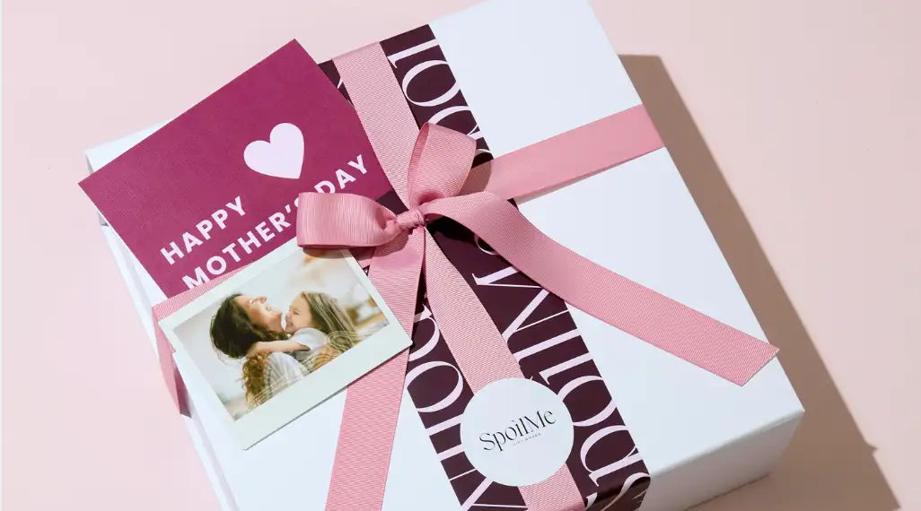 A white gift box adorned with a pink ribbon bow and maroon patterned wrapping paper, featuring the ’spoilme’ logo on a circular tag.