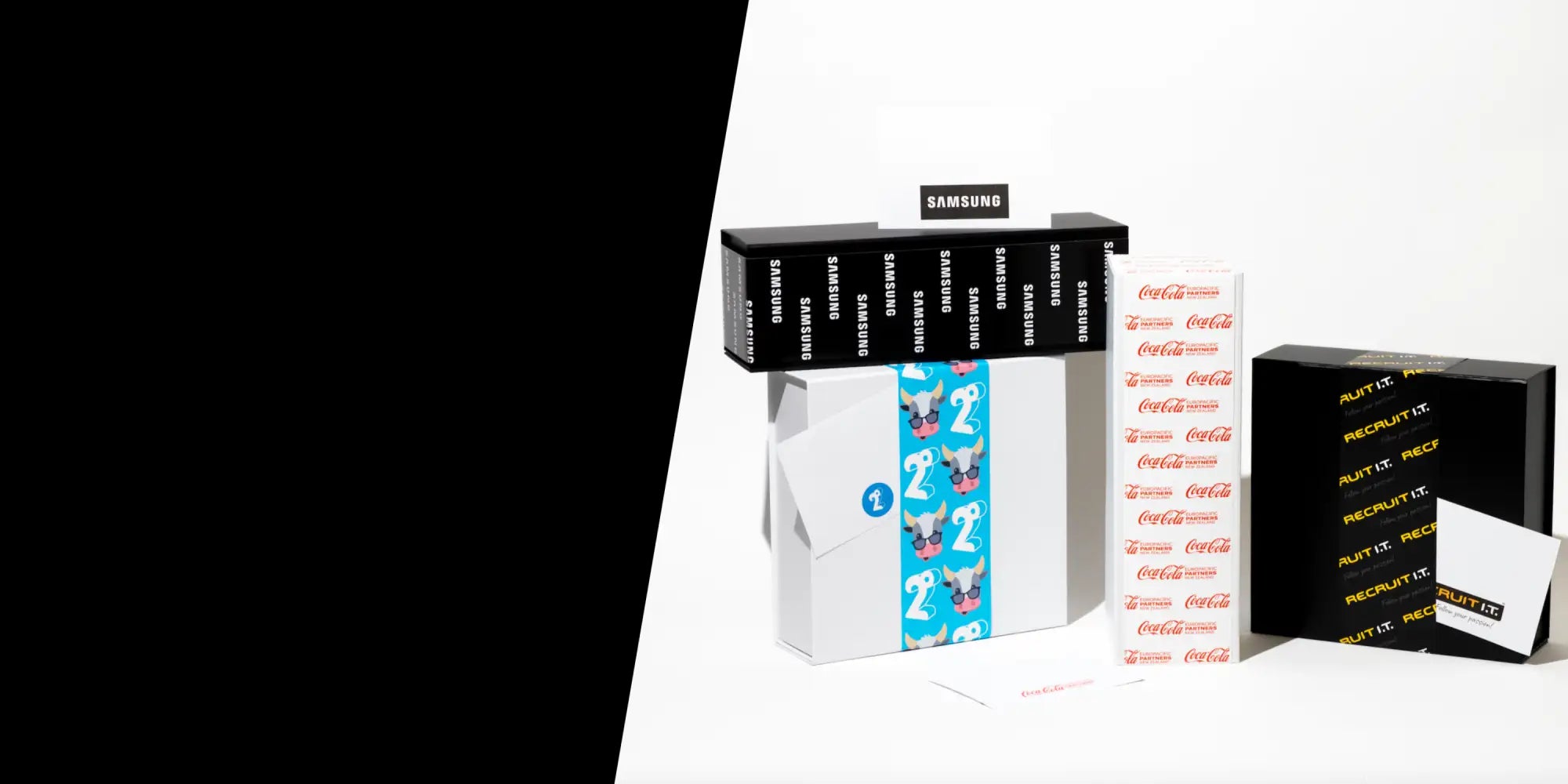 White rectangular box with blue vertical stripe featuring cartoon dog faces and a circular logo, positioned next to black boxes labeled ’samsung’ and ’recruit.it’.
